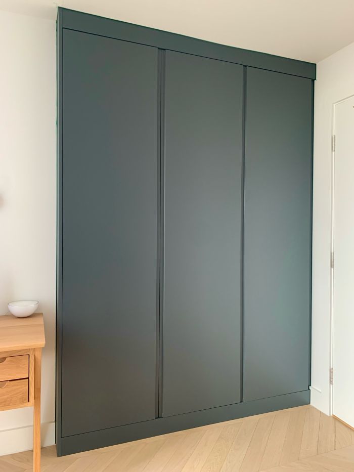Green handleless fitted wardrobe in a small bedroom